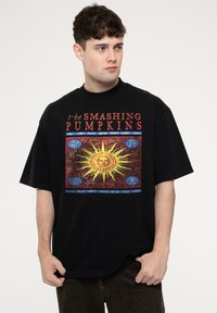 Black oversized t-shirt featuring a colorful sun graphic with intricate details and text reading "the SMASHING PUMPKINS." Cotton material.