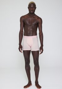 Lyserøde boxershorts lavet af glat stof, med en blød elastik i taljen, tætsiddende design og kontrastsyninger.