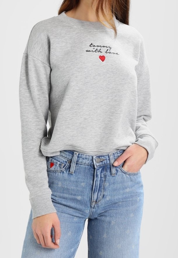 Sweat-shirt gris avec le texte « tommy with love » et une broderie cœur rouge, associé à un jean bleu clair avec un petit cœur rouge sur la poche.