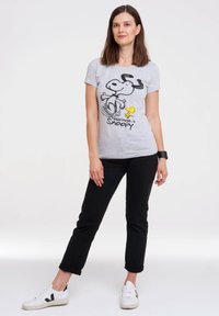 Gray t-shirt featuring a Snoopy graphic with black outlines and a yellow Woodstock, paired with black rolled-up jeans and white sneakers.