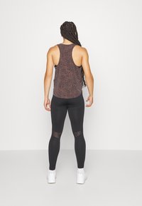 Hnědé tílko s leopardím vzorem a designem racerback, doplněné černými legínami s průhlednými vložkami na lýtkách. Bílé tenisky.