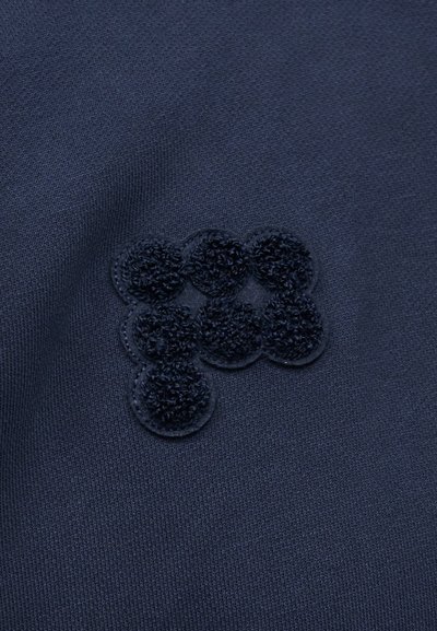 Tissu bleu foncé avec une application texturée en relief composée de six cercles superposés formant un groupe abstrait.