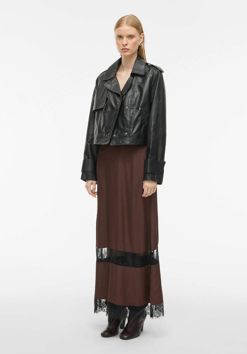 Juoda odinė trumpa striukė dėvima virš rudos maksi suknelės, kuri yra su juodu nėriniu. Blizgūs kulkšnies botai užbaigia įvaizdį. Lygūs tekstūrai, sluoksniuota dizaino.