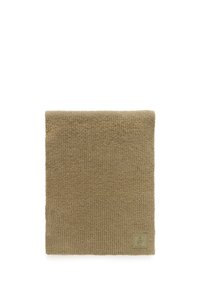 Strik en beige tørklæde med et struktureret mønster; har et firkantet logo-patch i nederste hjørne.