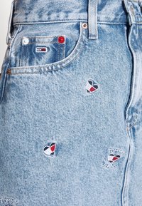 Vaqueros de mezclilla azul claro con pequeños diseños de corazones bordados en rojo, blanco y azul marino, con un bolsillo frontal y detalle de logo.