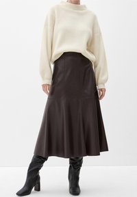 Suéter de canalé crema con un cuello alto, combinado con una falda de cuero marrón oscuro en línea A, y luciendo botas de tacón altas negras hasta la rodilla.