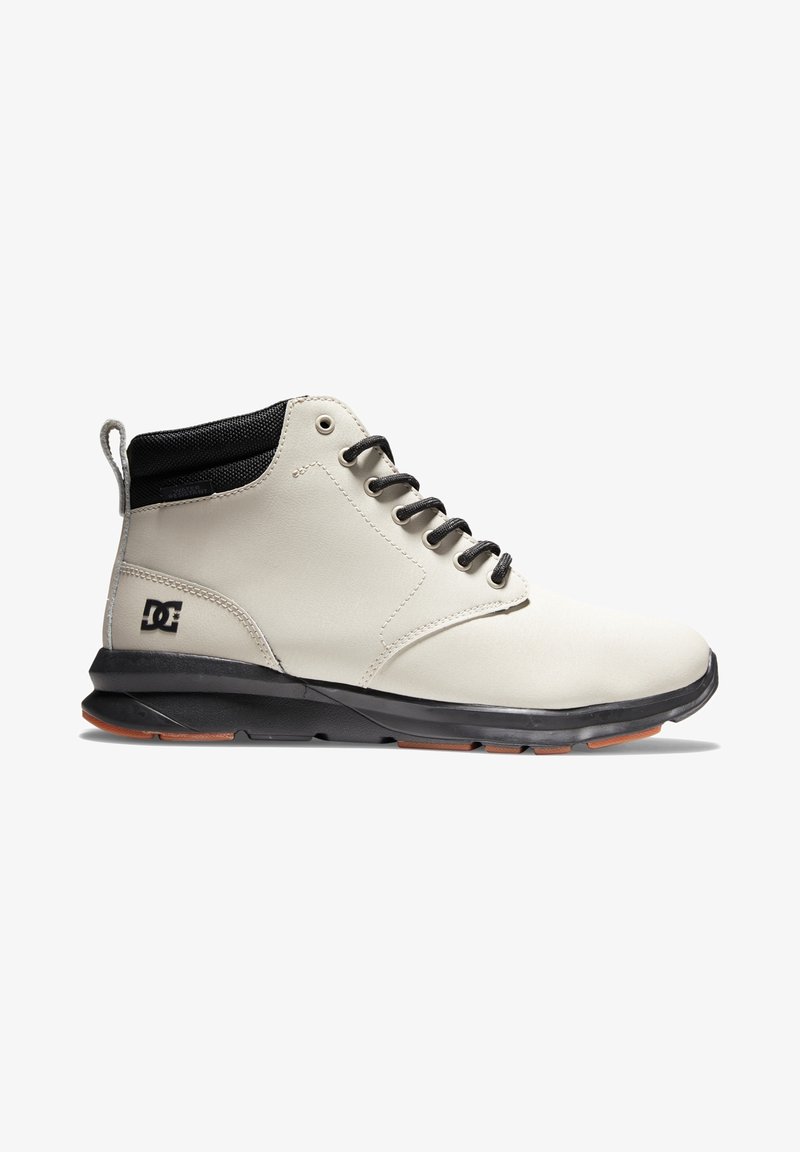 Baskets montantes beige clair avec col noir, lacets noirs, semelle noire et logo de la marque DC sur le côté du talon.