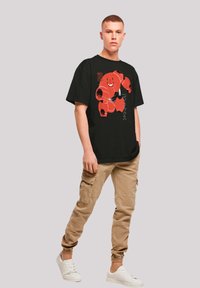 Schwarzes, übergroßes T-Shirt mit einem roten Cartoon-Charakterdesign. Kombiniert mit beigen Cargo-Hosen mit elastischen Bündchen und weißen Sneakers.