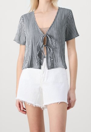 Schwarzes und weißes Gingham-Kurzarmoberteil mit tiefem V-Ausschnitt und Bindeband vorne. Kombiniert mit ausgefransten weißen Denim-Shorts.