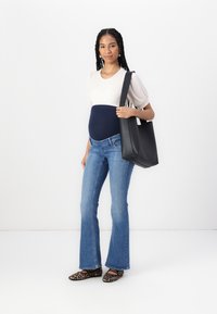Svart lær tote bag med en strukturert design, kombinert med en tettsittende ribbestrikket kremfarget topp og utsvingte blå jeans, med leopardmønstrede leiligheter.