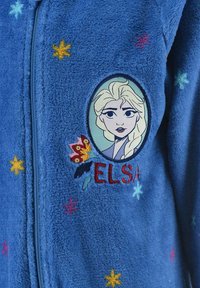 Sudadera con cremallera de felpa azul que presenta un parche bordado de Elsa rodeado de flores y estrellas de varios colores, y un tejido suave y texturizado.