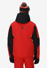 Giacca da sci rossa e nera con accenti arancioni, dotata di cappuccio, logo sulla schiena e maniche lunghe. Il tessuto sembra impermeabile e textured.