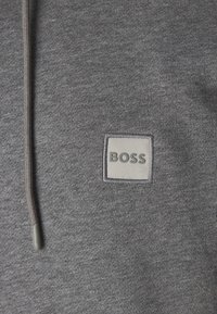 Gray sweatshirt featuring a textured fabric, with a square gray patch labeled "BOSS" in the center and a drawstring at the neckline.
