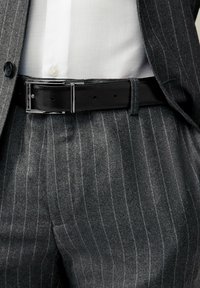 Pantalons en tissu rayé gris associés à une chemise blanche, rehaussés d'une élégant ceinture en cuir noir dotée d'une boucle en argent brillant.