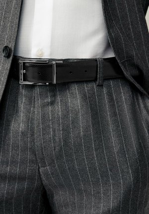 Szare spodnie w prążki zestawione z białą koszulą, podkreślone eleganckim czarnym skórzanym paskiem z błyszczącą srebrną klamrą.