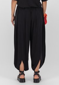 Svarta, löst sittande byxor med sidslitsar, tillverkade av mjukt tyg. Bärs med kraftiga svarta sandaler med justerbar rem.