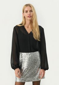 Blusa nera trasparente a maniche lunghe con scollatura a V abbinata a una mini gonna argentata con paillettes, che riflette brillantezza e texture.
