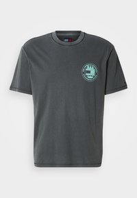 Σκούρο γκρι βαμβακερό t-shirt με κοντά μανίκια, στρογγυλή λαιμόκοψη και τιρκουάζ κυκλικό λογότυπο με κείμενο. Καθημερινό σχέδιο με απλή υφή.