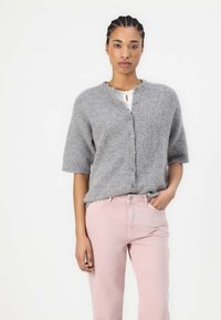 Gray knitted cardigan with short sleeves, button closure, worn over a white top, paired with light pink pants. Simple, textured design.