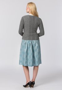 Grauer Strickpullover mit strukturiertem Rücken und einem hellblauen Rock mit Paisleymuster, kombiniert mit schwarzen High Heels.