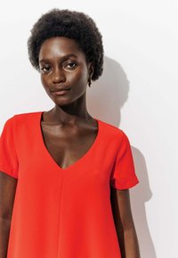 Robe rouge à manches courtes avec un décolleté en V, fabriquée en tissu lisse. Présente une coupe décontractée et une couture décorative sur le devant.
