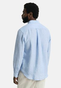 Lichtblauw langarmshirt van linnen, met een button-down kraag, een afgeronde zoom en een plooi detail aan de achterkant.