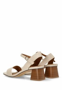 Sandalias de cuero beige con correa en el tobillo, punta descubierta y un tacón bloque a rayas marrón. La suela es de color claro y tiene una textura suave.