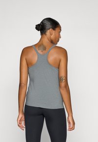 Grå atletisk tanktop med racerback-design, glatt tekstur og buet nedre kant, kombinert med svarte leggings. Synlige tatoveringer på ryggen.