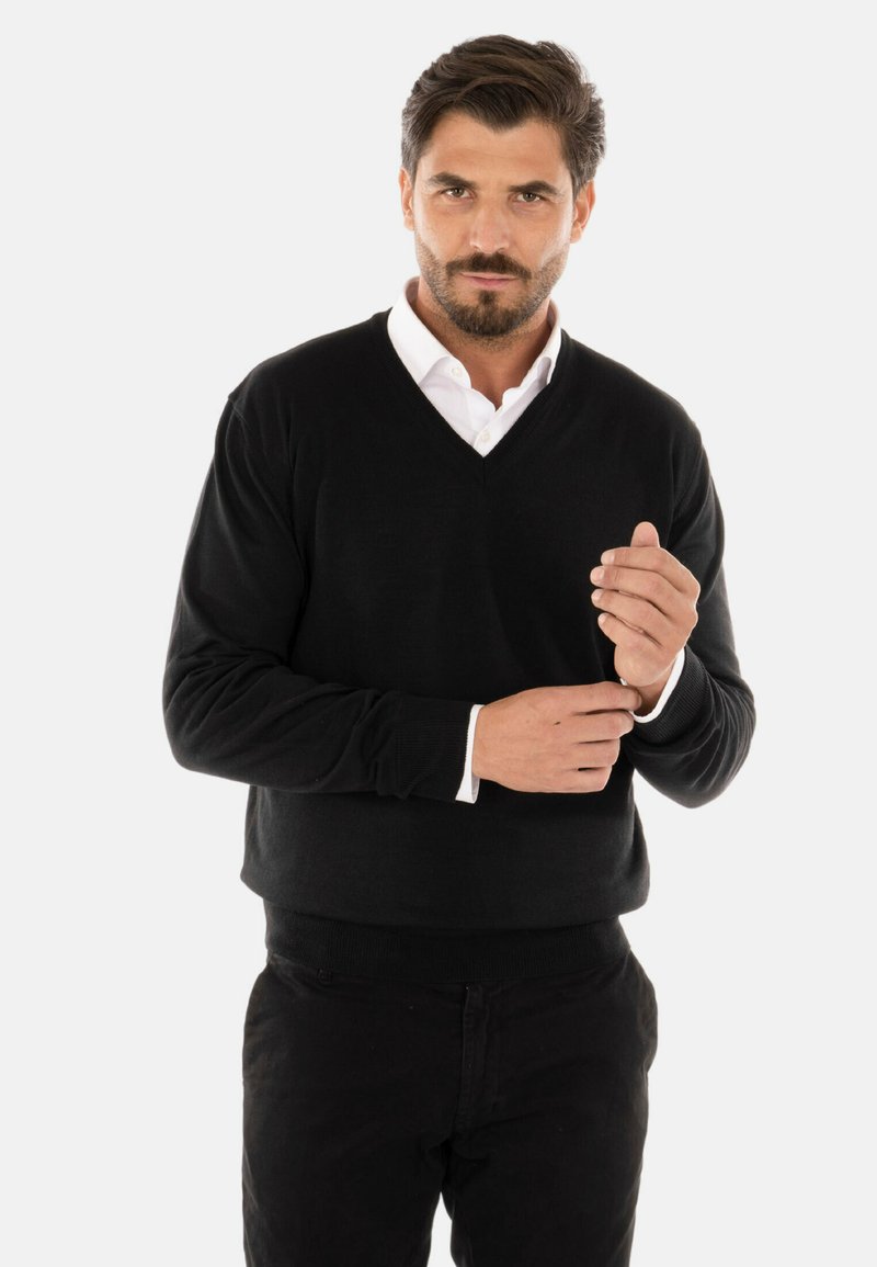 Maglione nero a V realizzato in tessuto a maglia. Caratterizzato da maniche lunghe, polsini a coste e una vestibilità comoda. Indossato sopra una camicia bianca con colletto.