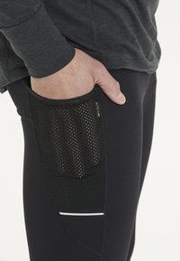 Sorte atletiske leggings med en mesh-lomme på siden, der har en subtil refleksaccent og glat, strækbart stof.