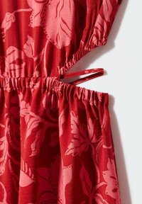 Tessuto a motivi floreali rossi con vita arricciata e dettaglio con cinturino. Il design include grandi foglie rosa e una texture liscia.