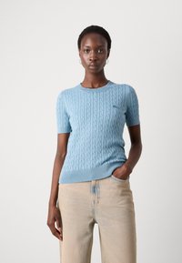 Maglione azzurro chiaro a maniche corte in maglia con motivo a treccia, colletto e orlo ribbed. Abbinato a pantaloni in denim chiaro.