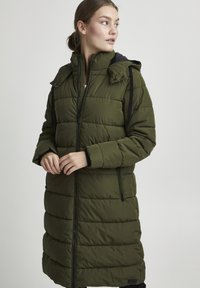 Olijfgroen pufferjack met een ritsafsluiting, zijzakken en een afneembare capuchon. Bevat verticale gestikte textuur en zwarte accenten.