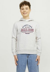 Pilkas džemperis su priekine kišenė ir raišteliu reguliuojama kapuce. Ant jo spausdintas logotipas "Jack & Jones" raudonai ir mėlynai. Nešiojamas su mėlynais džinsais.