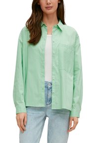 Groen gestreepte blouse met een zak, gemaakt van lichtgewicht stof. Heeft een relaxte pasvorm en lange mouwen. G draagt over een witte top.