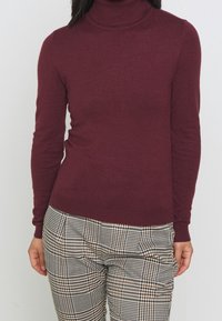 Burgundowy sweter z golfem, wykonany z miękkiego materiału, z długimi rękawami i dopasowanym krojem, zestawiony z w kratkę spodniami.