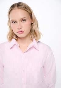 Light pink button-up shirt with white vertical stripes, a pointed collar, and a single chest pocket, made from woven cotton fabric.
