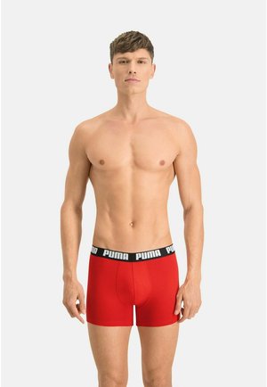 Young man with short hair wearing red Puma boxer briefs with black waistband, standing against a plain light background.