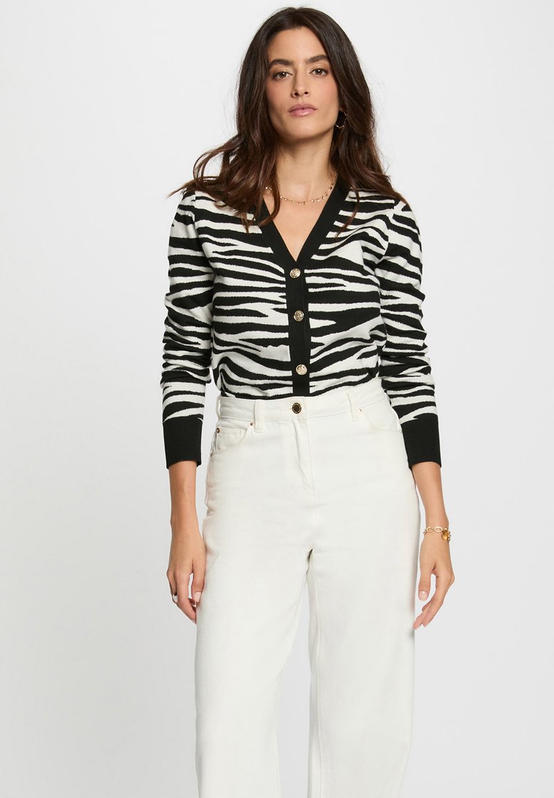 Cardigan à motif zèbre noir et blanc avec un col en V, un devant à boutons et des poignets côtelés, associé à un pantalon large taille haute blanc.