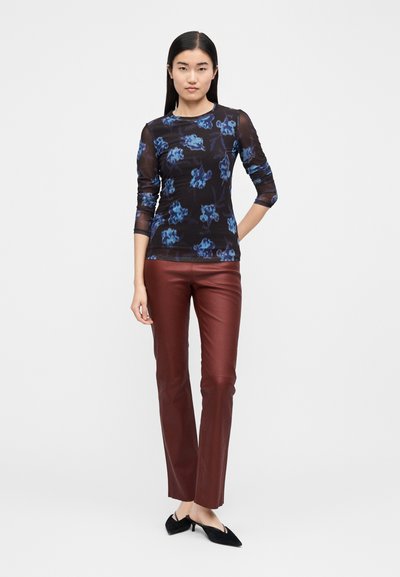 Long-sleeve mesh top with blue floral print on a black background, paired with fitted burgundy faux leather pants and black heels.
