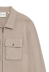 Beige zip-up jacka med krage, har en enskild bröstficka, silverdragkedja och en mjuk tygtextur.