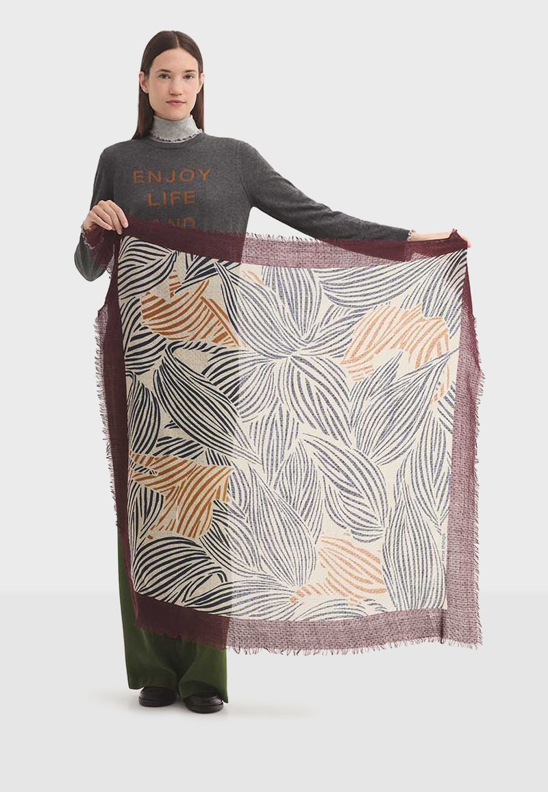 Gran bufanda rectangular con un diseño floral que incluye hojas en colores azul marino, naranja y beige sobre un fondo crema, bordeada por un fleco burdeos.