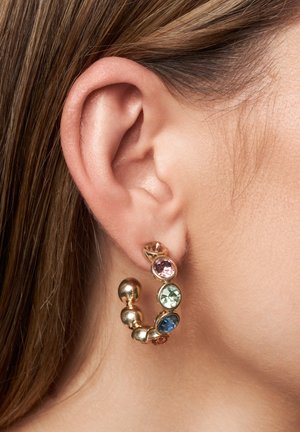 Pendientes de aro de oro que presentan coloridas piedras preciosas, con una superficie lisa y pulida y acentos esféricos, exhibidos en la oreja de un modelo.