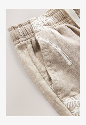 Pantaloncini beige in lino con vita elastica, caratterizzati da motivi ricamati bianchi e tasche. Tessuto testurizzato con dettagli di cuciture visibili.