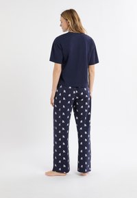 Granatowy bawełniany T-shirt z krótkimi rękawami w komplecie z wzorzystymi spodniami do spania z nadrukiem białych psów, gładką teksturą i luźnym krojem.