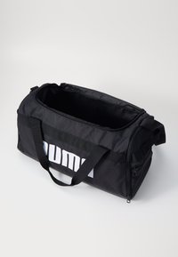 Zwarte sporttas gemaakt van duurzaam stof, met een groot wit logo, dubbele handvatten, een rits aan de bovenkant en een ruime binnenkant.