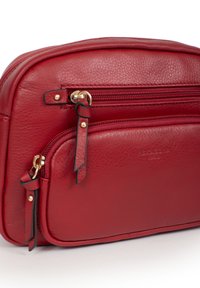 Borsa in pelle rossa con doppi scomparti zip, dettagli in metallo dorato e texture liscia. Nome del marchio impresso sulla parte anteriore.