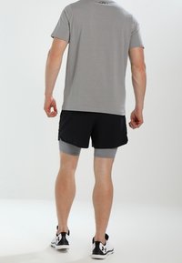 Camiseta gris de manga corta, pantalones cortos negros con un forro interno gris, combinados con zapatillas deportivas blancas. Diseño simple, tejido transpirable y ajuste funcional.