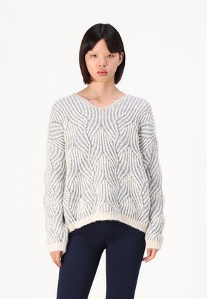 Chunky knitted sweater in cream with blue wave patterns, V-neck, long sleeves, and ribbed hem; soft texture, relaxed fit.