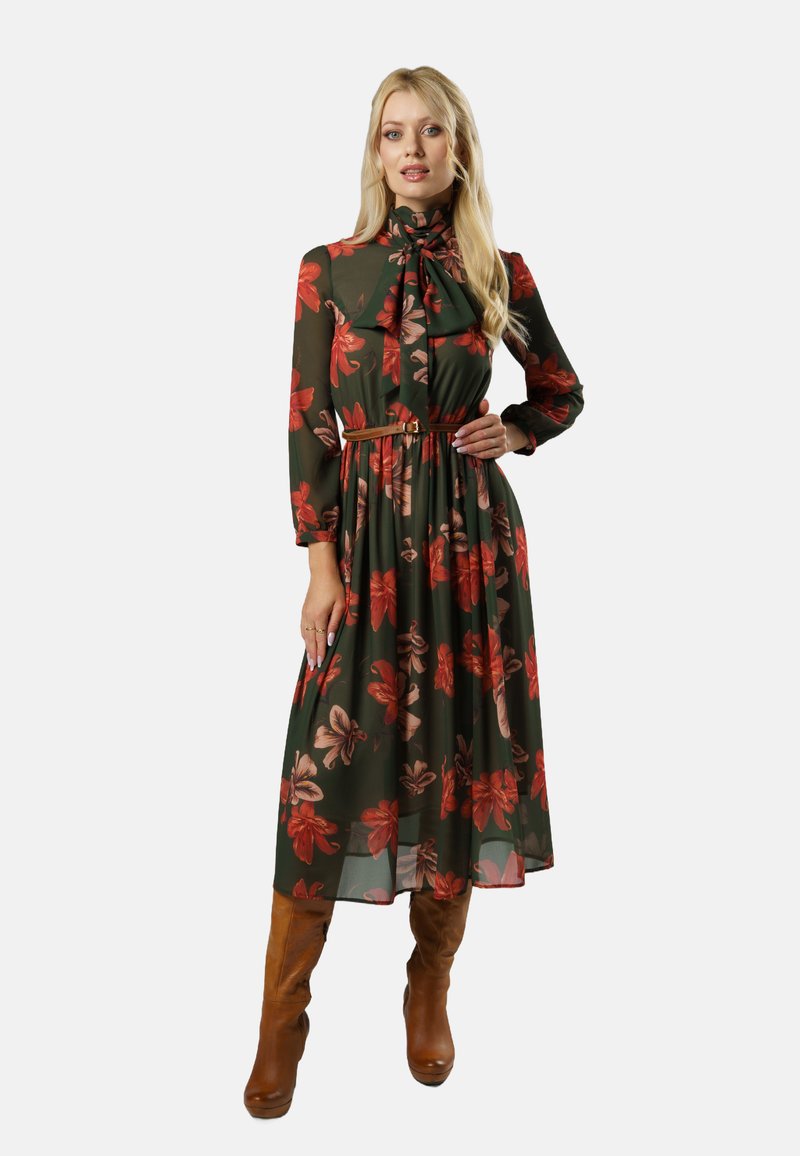 Kwiatowa długa sukienka w ciemnozielonym kolorze z czerwonymi i beżowymi wzorami kwiatowymi. Posiada wysoki dekolt, długie rękawy oraz dopasowaną talię z paskiem.